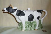 Large black and white cow creamer filled below with gress